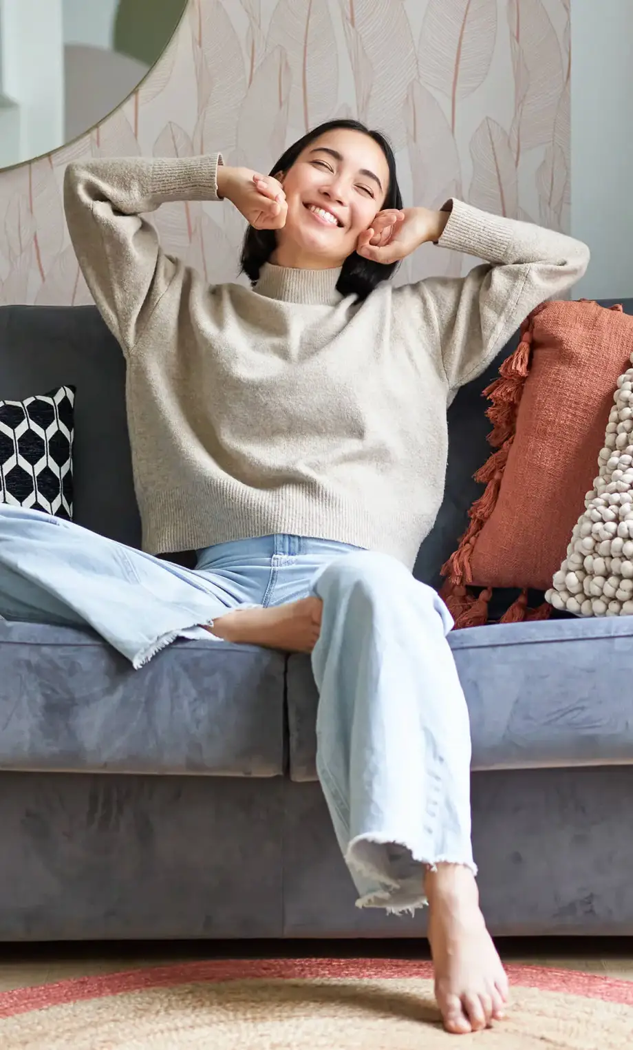 Portrait of happy asian woman feeling lazy, stretching on sofa and smiling pleased, relaxing at home, resting from work.